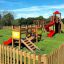 Wooden playground Mini play with slides, climbing structures, and swings in a fenced grassy area.