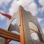 Tintagel playground castle with red flag and wooden elements, against blue sky with clouds.