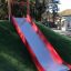 Red and silver playground Slide on a grassy hill.