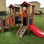 Outdoor playground with a red slide, climbing section, and playhouse features.