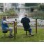 Two elderly people using the Training twist & sit exercise equipment in a park by a fountain.