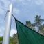 Sun Shade Triangle 5x5x5 Atlantis (Metal) installed on a pole outdoors with a blue sky and trees in 