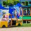 Child playing in a yellow Taxi playground vehicle near a green play train.