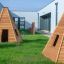 Wigwam wooden house on green grass near modern buildings