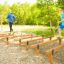 Two men running on wooden beams obstacle course 'Hip Hop' in an outdoor playground.