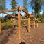 Wooden climbing obstacle ladder in an outdoor play area surrounded by trees.