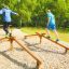 Two people balancing on the Easy Balancer outdoor fitness equipment in a park.
