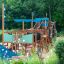 Wooden playground structure Majestic ship with slide with blue accents in a green park setting.