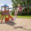 Two children playing on a Double Swing with Tower playhouse with slide on a sunny day.