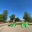 Green playground equipment called Umbrella with sunshade and seating on sandy ground.
