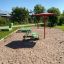 Green playground structure with a red Umbrella on sandy ground.