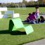Green lounge chair on a playground lawn with children playing in the background