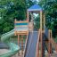 Twister castle with slide in a playground with sand base and greenery in the background.