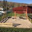 Double Swing (BNS 90cm) in a sand playground with wooden fencing and a red building in the backgroun
