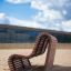 Sofa Wave, modern outdoor wooden bench on sandy surface in urban environment.
