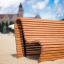 Wooden Sofa Wave bench on sandy beach with building in background.