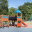 Square Play castle with slide in a playground with trees in the background.