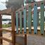 Square Play castle with slide on a sandy playground near a lake surrounded by trees.