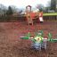 Alien rocking playground equipment with bright green arms and central round seat in a bark-covered p