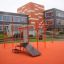 New Age Fit MEDIUM outdoor fitness station with orange structures in front of a modern building.