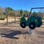 Green Double Auto rocking toy in a playground with a wooden structure and swings in the background