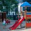 Two girls at a playground with a red slide and a Mini Tractor rocking.