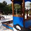 Villa with Orca single playhouse in a sandy playground area with surrounding trees.
