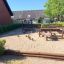 Natural play area 'Poison Ground' with wooden structures and sand in a residential neighborhood.