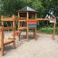 Six Angle with Suspension Bridge single slide wooden playground set in a sandy play area.