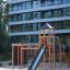 Explorer castle with slide wooden playground structure on sandy area in front of modern building