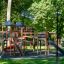 Large wooden playground structure with multiple slides and climbing areas in a park