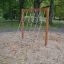 V-shape Net wooden playhouse in a sandy play area surrounded by trees.