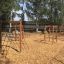V-shape Net wooden playhouse in a playground with climbing nets and wood chip flooring.
