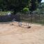 Single Seesaw in a sandy playground area surrounded by a wooden fence.