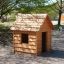 Wooden Nature Playhouse in playground surrounded by trees.