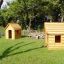 Two wooden Nature Playhouse structures on grass with trees in the background.
