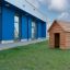 Wooden Nature Playhouse on grassy lawn in front of modern blue building.