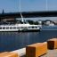 Wooden Cube benches along a waterfront promenade with a bridge and a boat in the background.