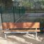 HPL Bench in a park setting with metal legs and wooden seat and backrest.