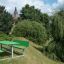 Green outdoor Table & Bench HPL set in a lush park with trees and a tower in the background.