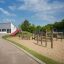 Playground equipment Somersault Triple with wooden structures and a red slide in a sandy area.