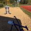 Outdoor gym equipment 'Double Ski Trainer' in a park near a running track.