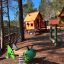 Olle's Playhouse: Wooden playhouse with slide and green spring rider in a forest-themed playground.