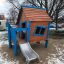 Olle's Playhouse wooden playhouse with blue accents and slide in a snowy park.