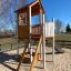 Wooden playhouse with ladder and slide in outdoor playground
